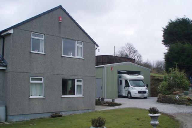 A two-storey house next to a green building containing a motorhome