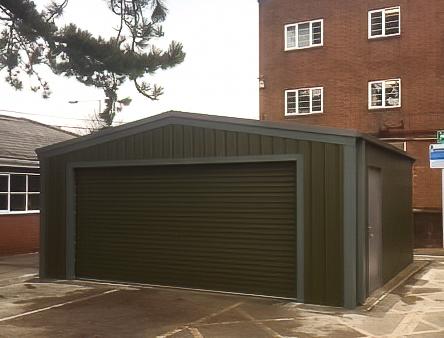 Exterior of a dark green steel garage with a wide roller shutter door and a side personnel door, situated in front of a brick building.