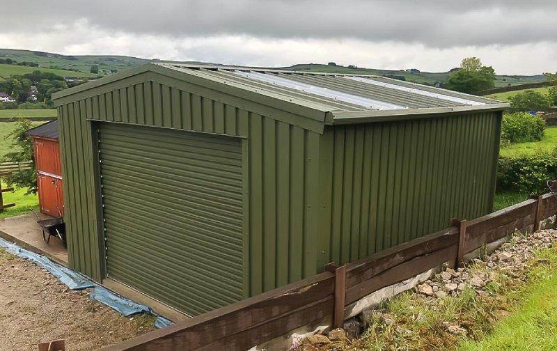 Angled view of an olive green steel building showing the roofline with integrated translucent skylight panels and a roller door.